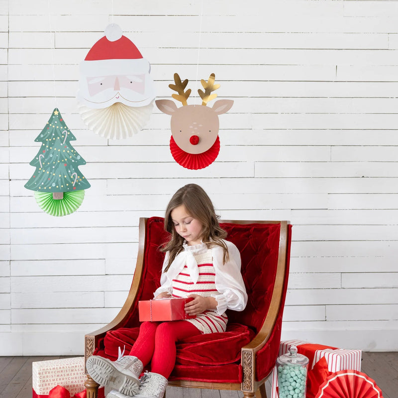 Lifestyle scene—girl in red chair under Santa, reindeer, and tree Christmas wall decor