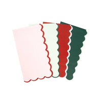 Four solid scalloped guest towels fanned out — pink, pale green, red, and dark green — each with a contrasting scalloped edge.