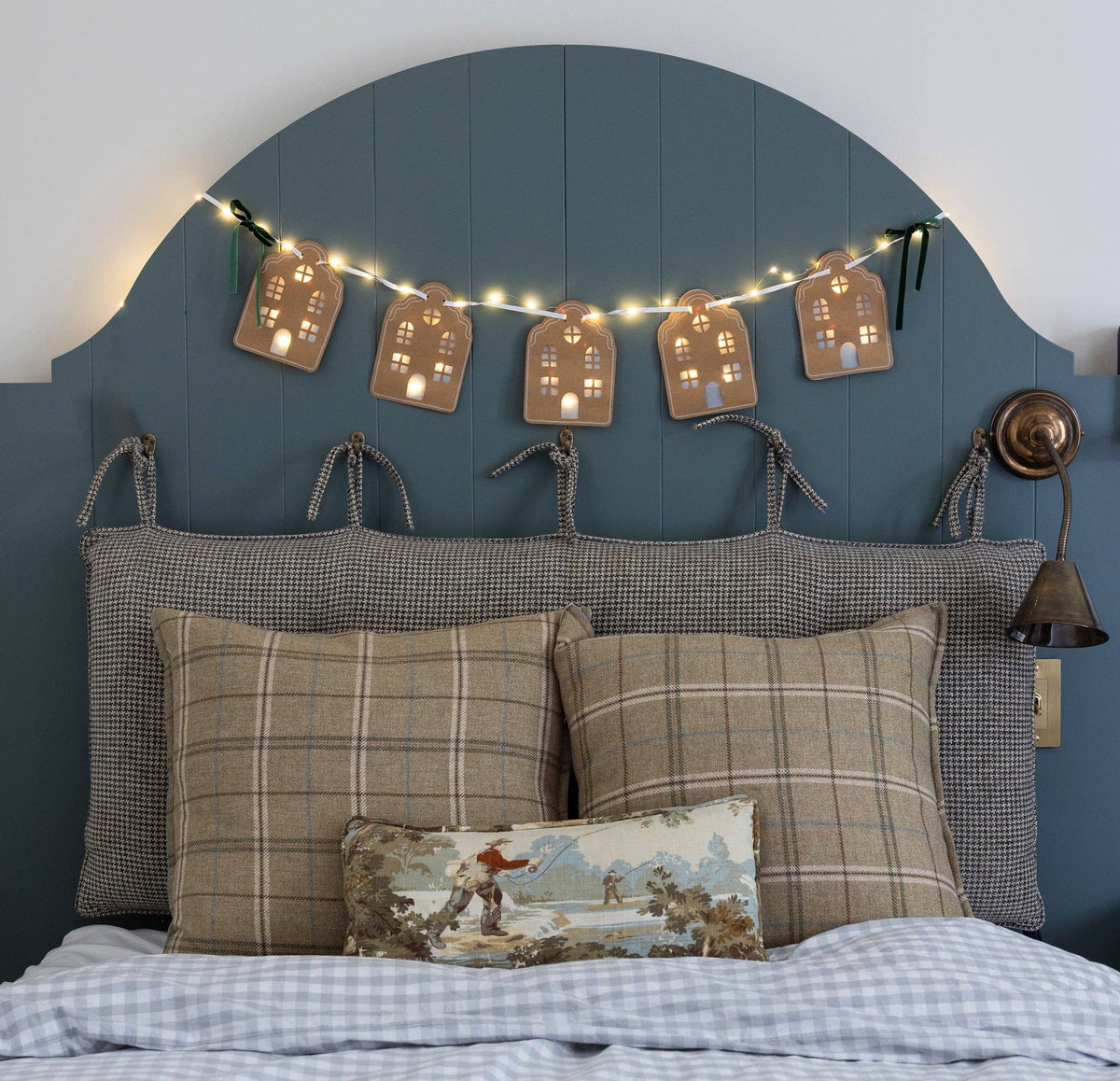 The lit house garland glowing above a bed headboard with plaid pillows.