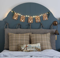 The lit house garland glowing above a bed headboard with plaid pillows.