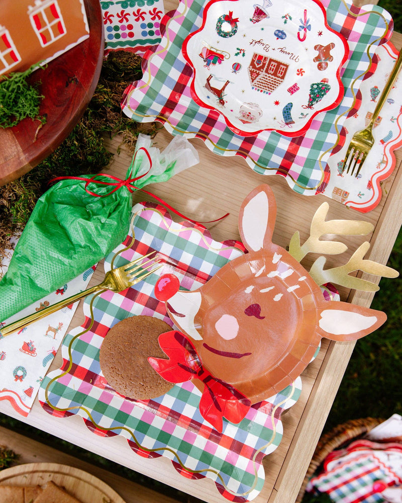 Merry + Bright Christmas icon paper plate on a gingham plate beside a reindeer plate and Christmas icon napkins; gingham plates, reindeer plate, napkins, fork, and piping bag shown separately, not included