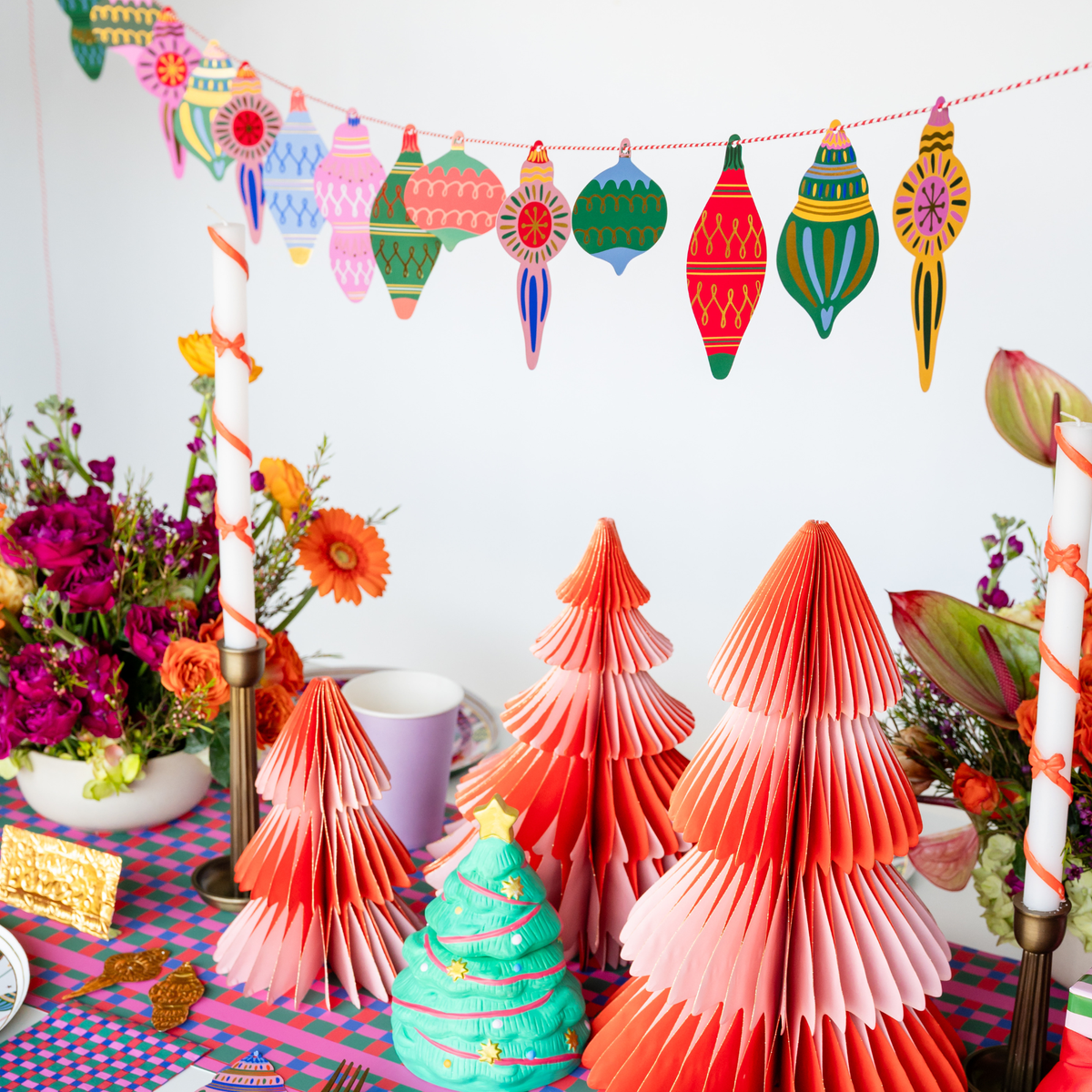 Styled holiday scene showing the ornament garland hung above pastel fabric Christmas trees, candy canes, and colorful holiday décor.