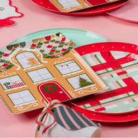 Place settings with red and mint dotted Christmas paper plates layered under gingerbread house plates.