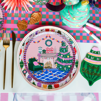 Overhead holiday place setting showing the ornament napkin with ornament-patterned plates, a Christmas tree plate, gold flatware, and a paper fan.