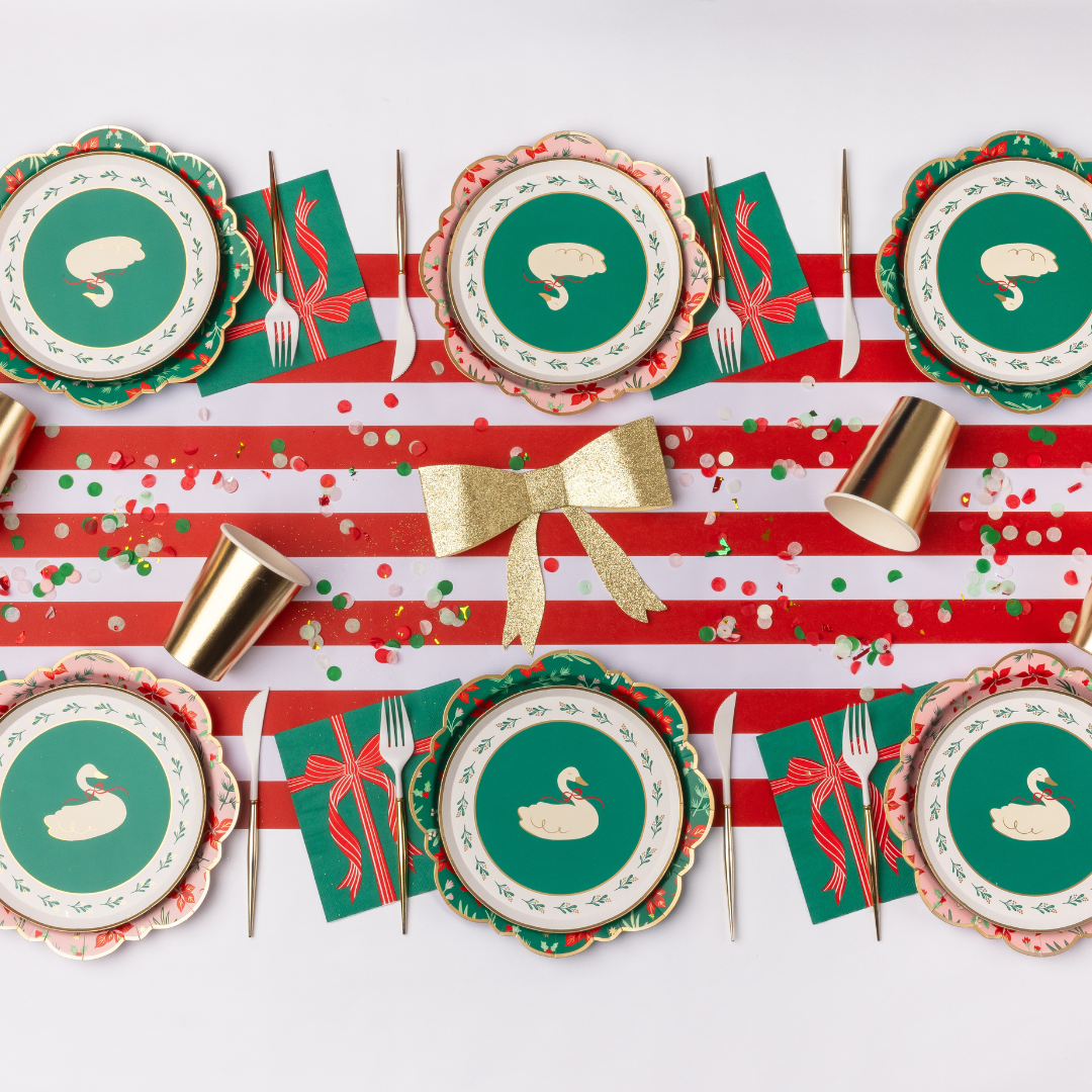 Styled holiday tablescape showing the green floral plates with coordinating wreath small plates, red-and-white striped runner, napkins, and a gold bow.