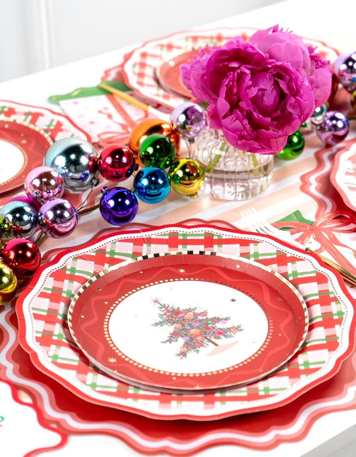 Overhead of a Christmas-tree plate on the plaid dinner plate with multicolor ornaments and pink peonies.