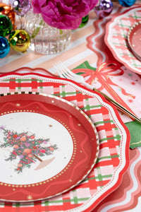 Place setting with a Christmas-tree plate on the plaid dinner plate, a striped runner, and a gold fork with a red bow.