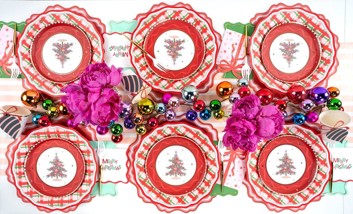 Overhead of Christmas-tree plates on plaid plates with pink peonies and multicolor ornaments.