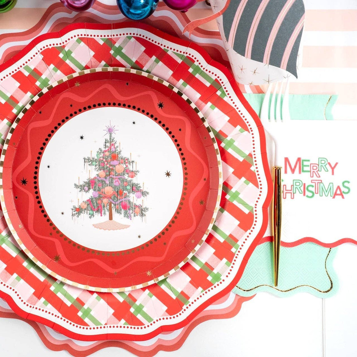 Place setting with a Christmas-tree plate on the plaid dinner plate and red scalloped charger with a "Merry Christmas" napkin.