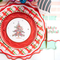 Place setting with a Christmas-tree plate on the plaid dinner plate and red scalloped charger with a "Merry Christmas" napkin.
