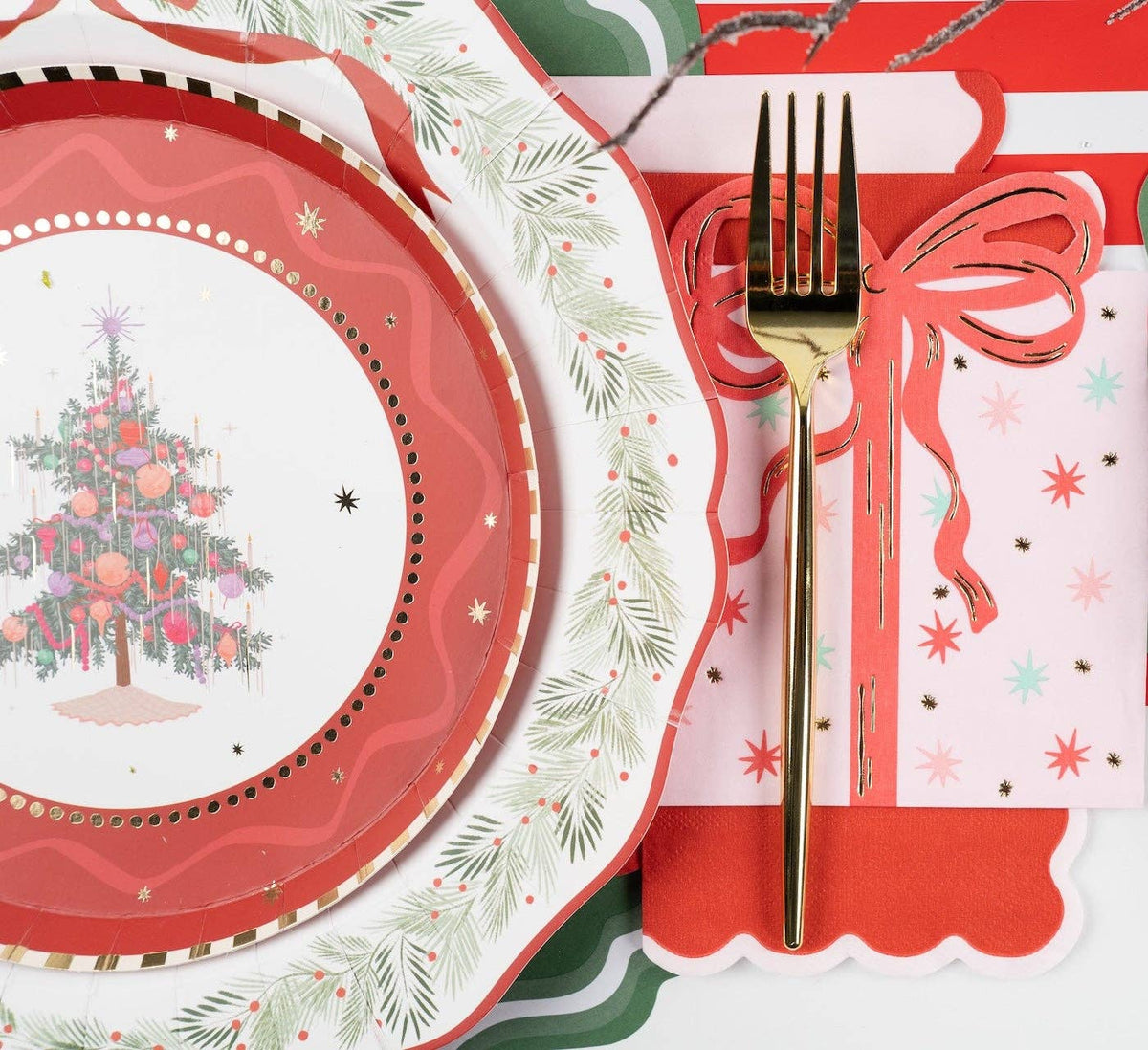 Place setting with a pink Christmas-tree plate, red scalloped border and holly rim, gold fork, and a pink star-print scalloped guest towel.