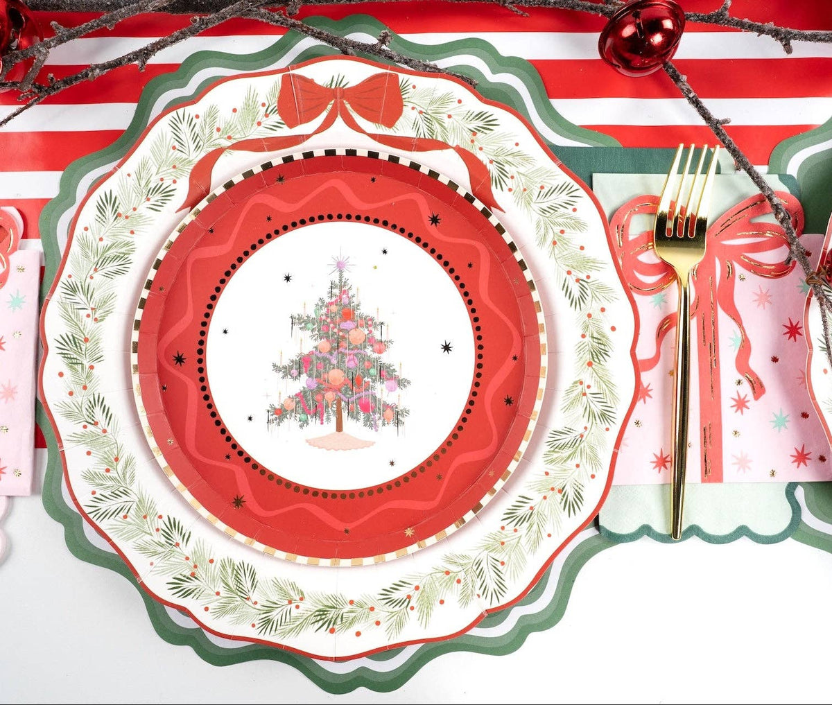 Vintage Christmas-tree plate on a red scalloped charger with a holly rim, a red ribbon bow, gold fork, and a pink star-print guest towel.