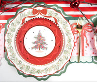 Vintage Christmas-tree plate on a red scalloped charger with a holly rim, a red ribbon bow, gold fork, and a pink star-print guest towel.
