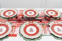 Overhead holiday table with multiple Christmas-tree medallion settings, green scalloped chargers, a striped runner, red ornaments, and gold cutlery.