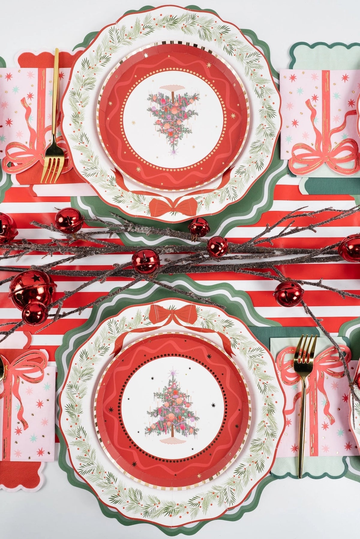 Overhead of several settings with tree plates on wreath dinner plates and green chargers, a striped runner, and red ornaments.