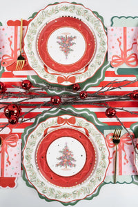 Overhead of several settings with tree plates on wreath dinner plates and green chargers, a striped runner, and red ornaments.
