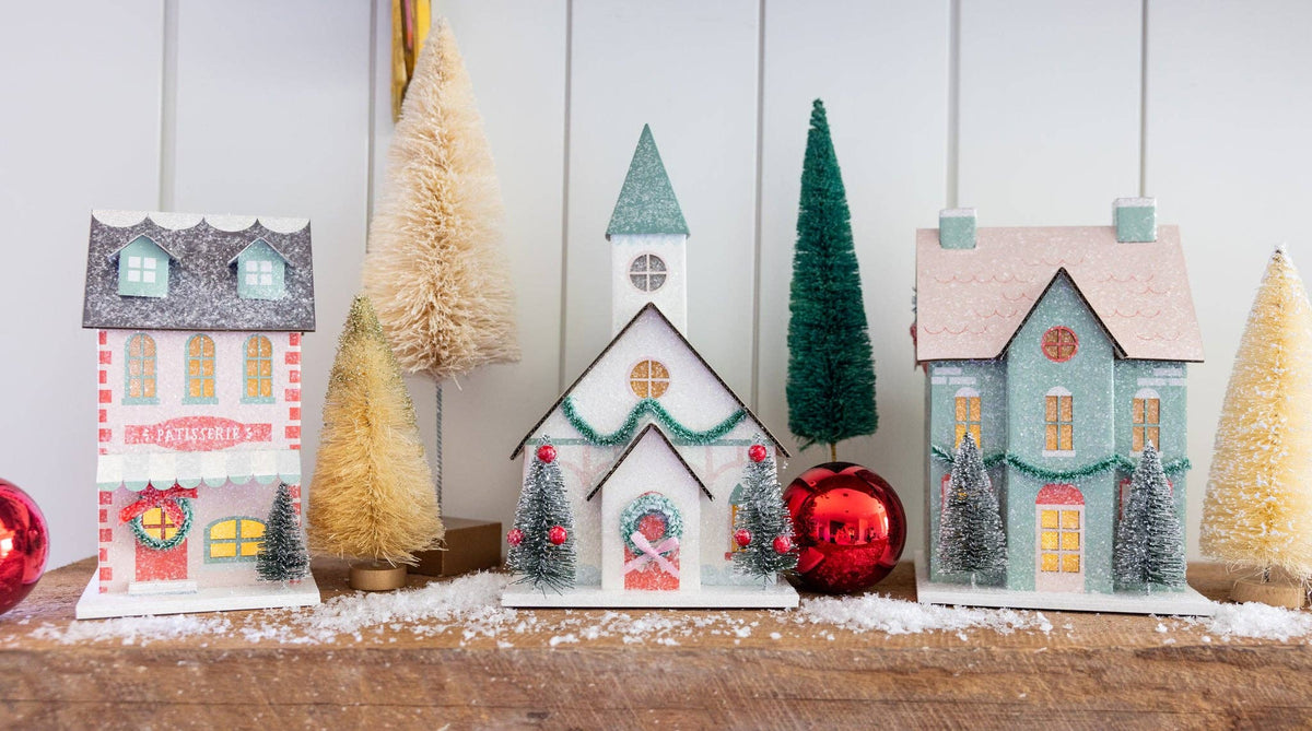 Christmas village mantel scene with a patisserie, church, and mint house among bottle brush trees and red ornaments