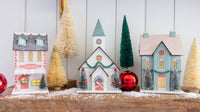 Christmas village mantel scene with a patisserie, church, and mint house among bottle brush trees and red ornaments