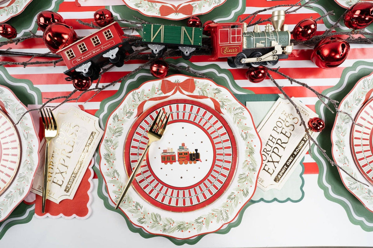 Overhead with a house-and-village medallion plate, green scalloped rim, toy-train decor, a striped runner, and "Express" gift-tag place cards.