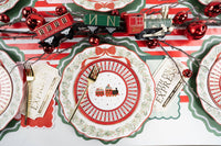 Overhead with a house-and-village medallion plate, green scalloped rim, toy-train decor, a striped runner, and "Express" gift-tag place cards.