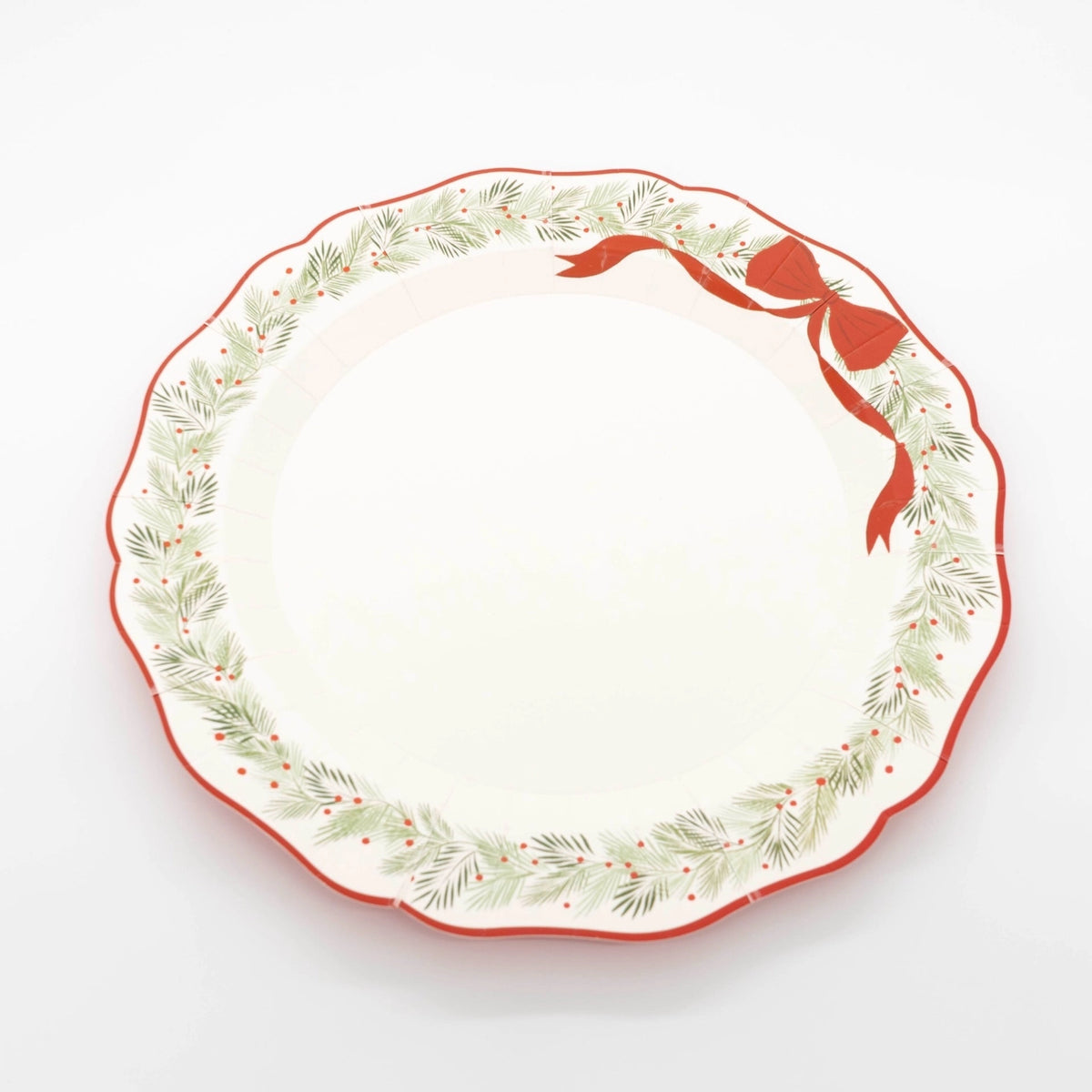Angled view of the wreath dinner plate showing the scalloped red rim and evergreen wreath.