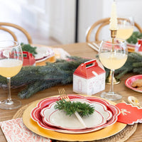 A beautifully set holiday table featuring the Christmas party paperware plates and glassware, illuminated by a candle.