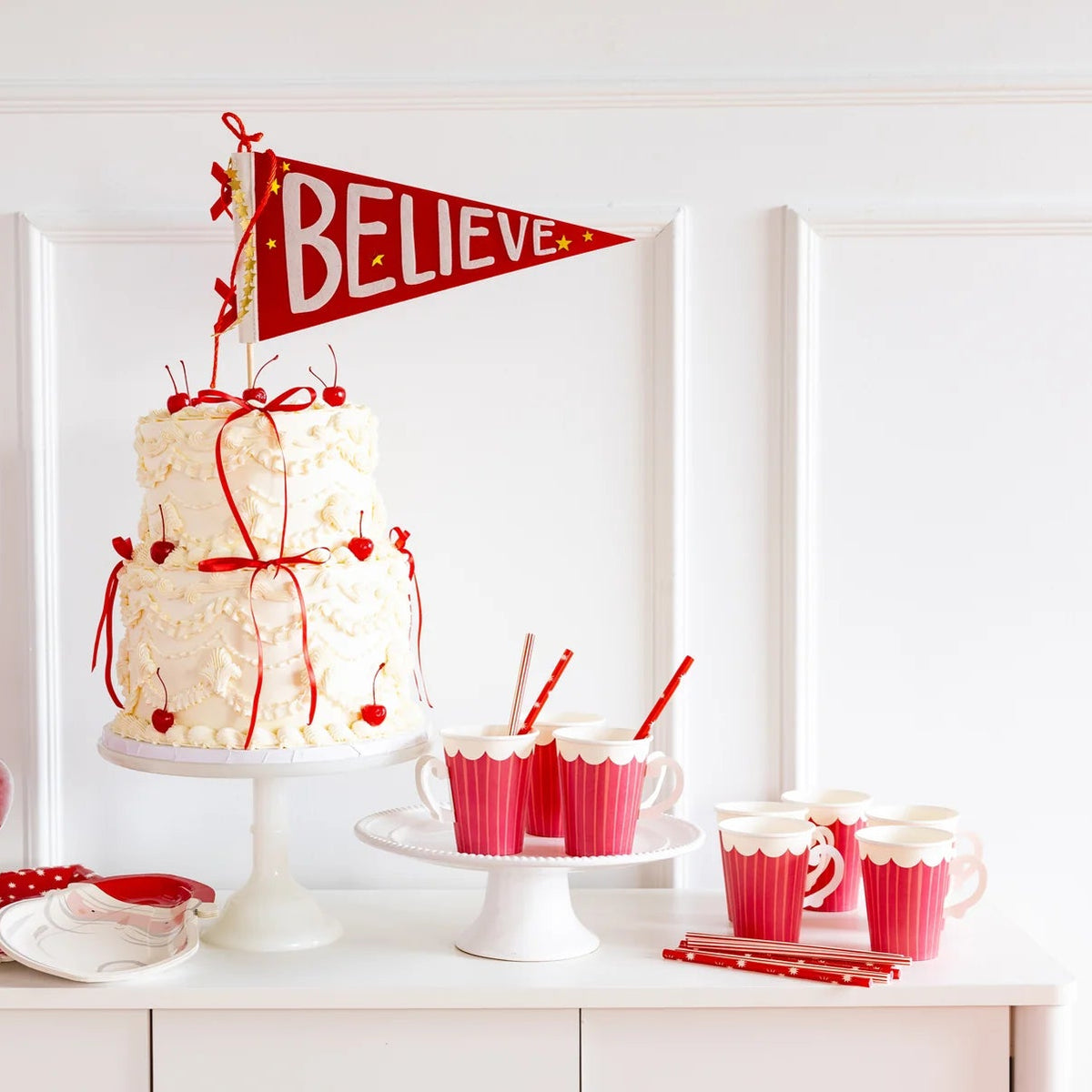 Festive Christmas table setting with white cake, red candy, and cups featuring the red straws and Believe banner.