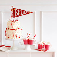 Festive Christmas table setting with white cake, red candy, and cups featuring the red straws and Believe banner.
