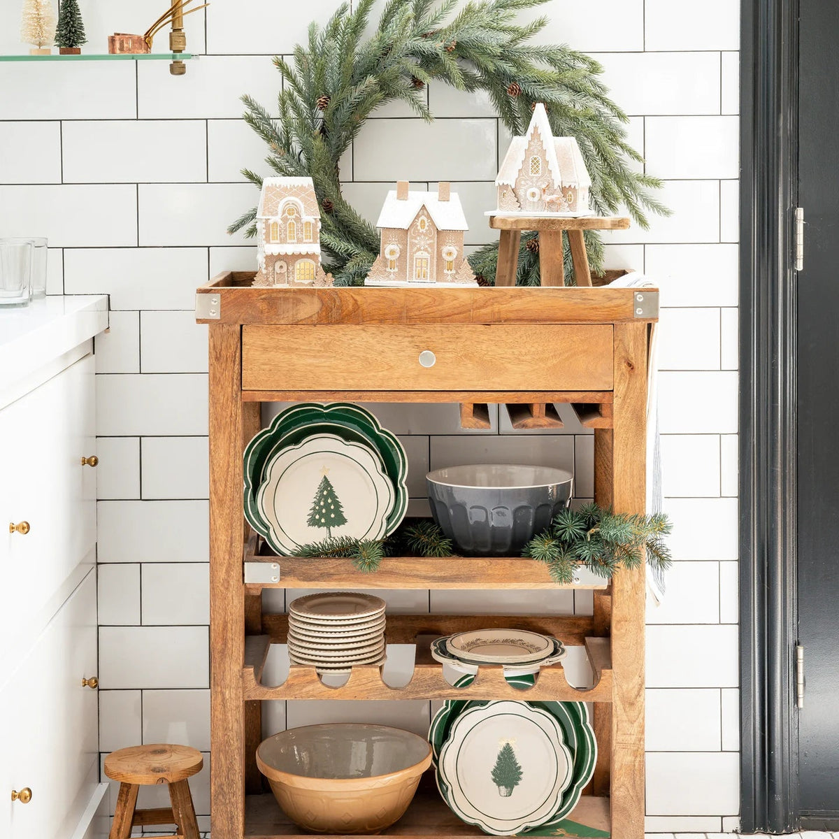 Christmas village display featuring the gingerbread house collection styled on a wooden bar cart with a green wreath.