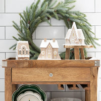 Christmas village display featuring the gingerbread house putz house set arranged around a green wreath and styled on a wooden cart.