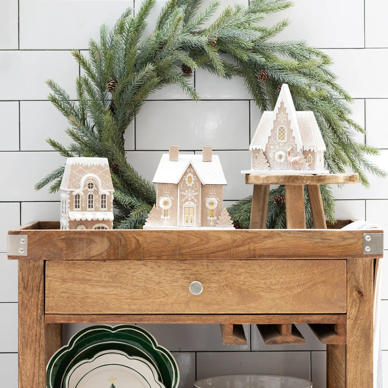 Christmas village display featuring the gingerbread house putz house set arranged around a green wreath and styled on a wooden cart.