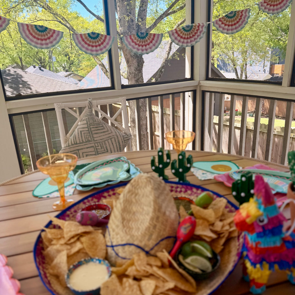 Cinco de Mayo fiesta tablescape on a screened porch with striped fan banner, sombrero paper plates, avocado napkins, chips and salsa, and mini piñata