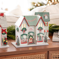 Close-up of the lighted holiday house storefront, showing the warm interior glow and exterior bottlebrush tree decor.