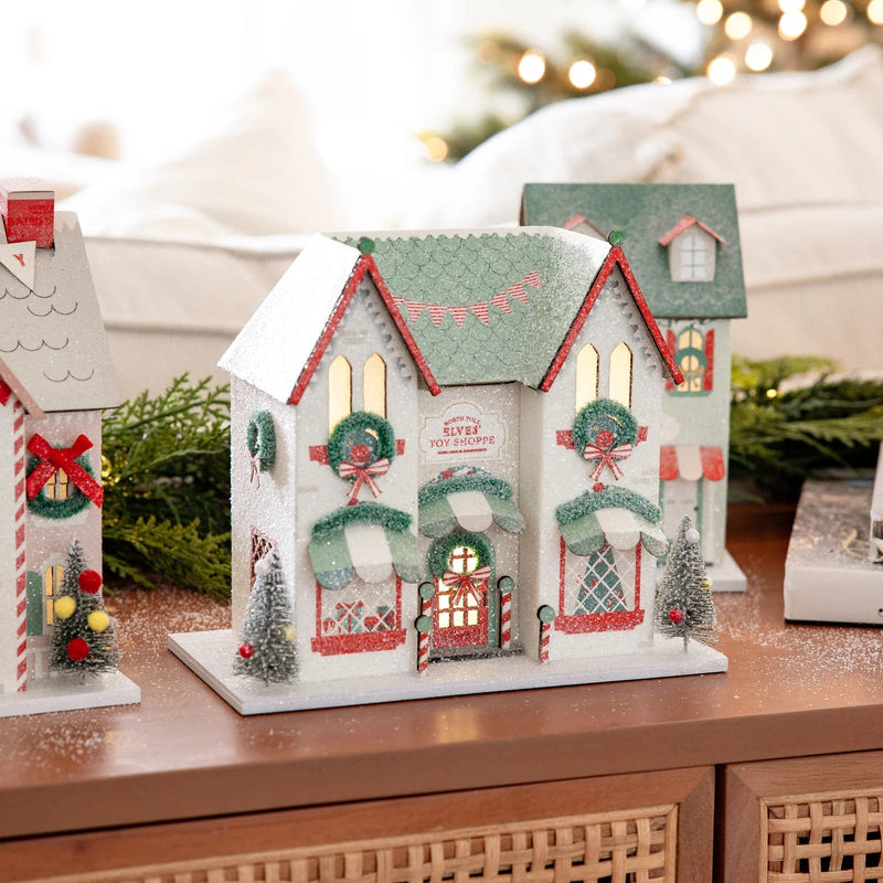 Close-up of the lighted holiday house storefront, showing the warm interior glow and exterior bottlebrush tree decor.
