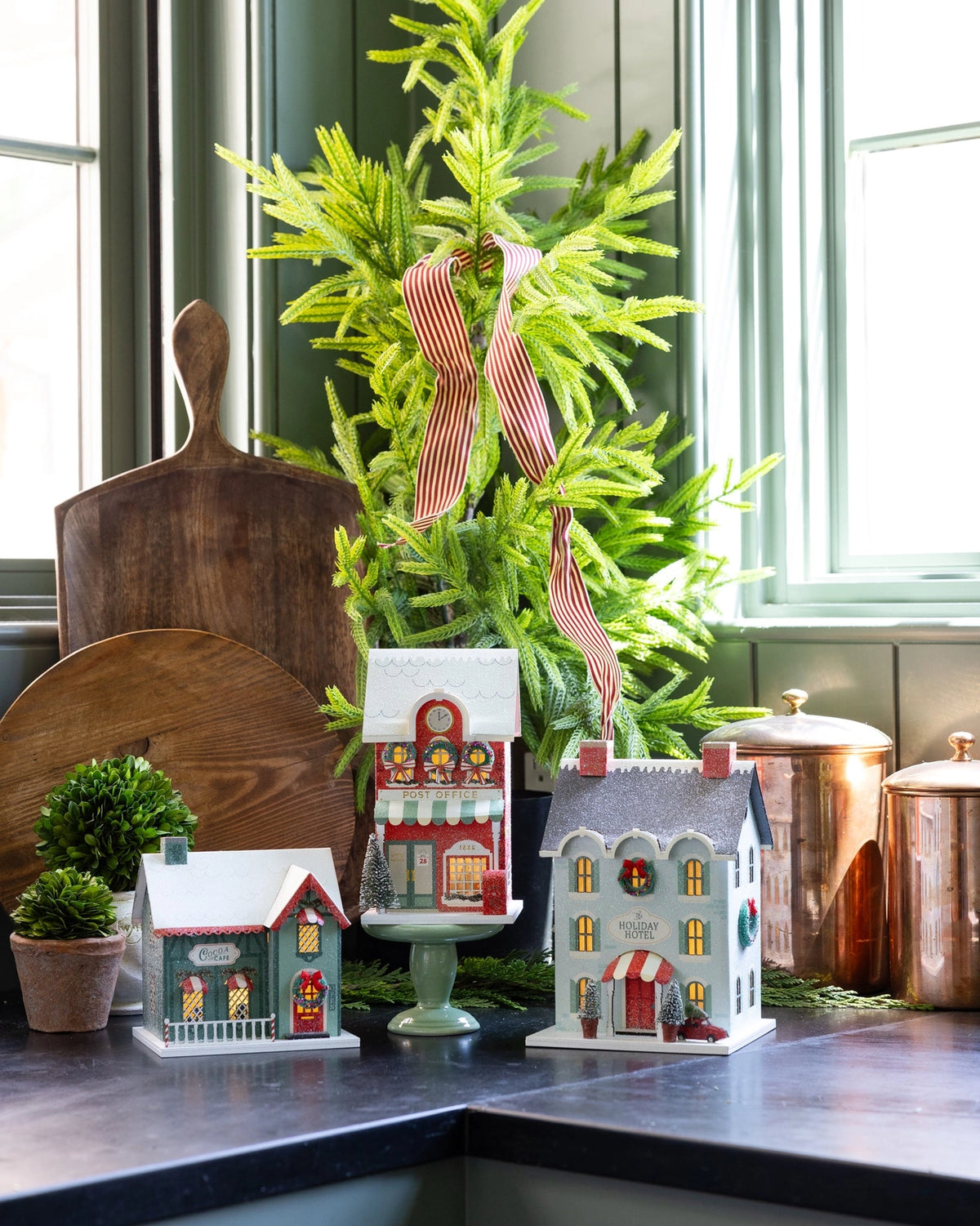 Three light up Christmas village buildings styled on counter with cocoa cafe in front left