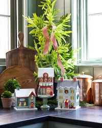 Three light up Christmas village buildings styled on counter with cocoa cafe in front left