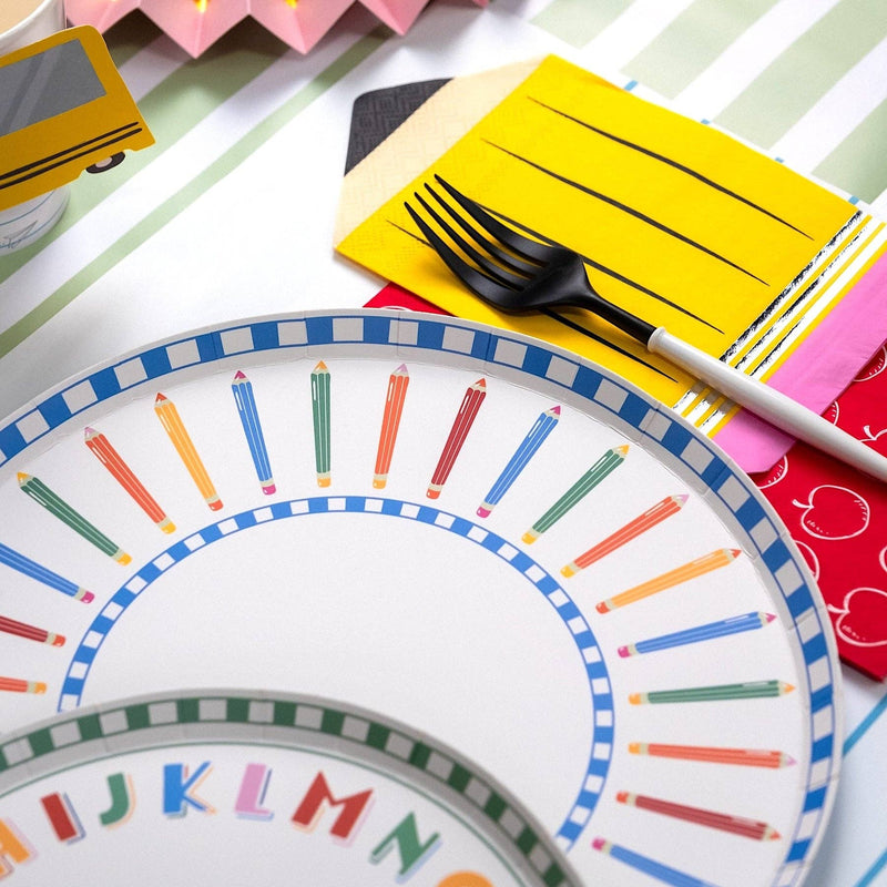Close-up of a colored pencil paper plate edge layered with an ABC alphabet paper plate edge, a yellow pencil-shaped napkin, and a red apple-print napkin