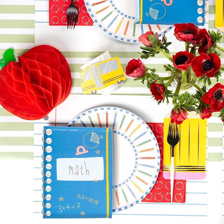 Place setting overhead with a colored pencil paper plate, math notebook-shaped napkin, school bus paper cup, red apple honeycomb decoration, pencil-shaped napkin holding black flatware, and red anemones