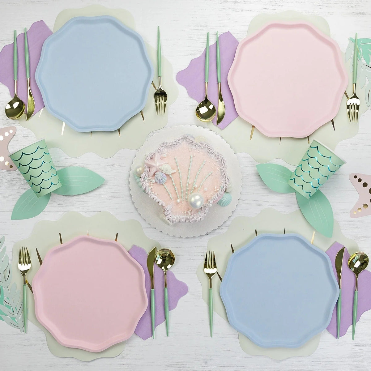 Four-place layout mixing sky blue and pink compostable plates around a shell cake.