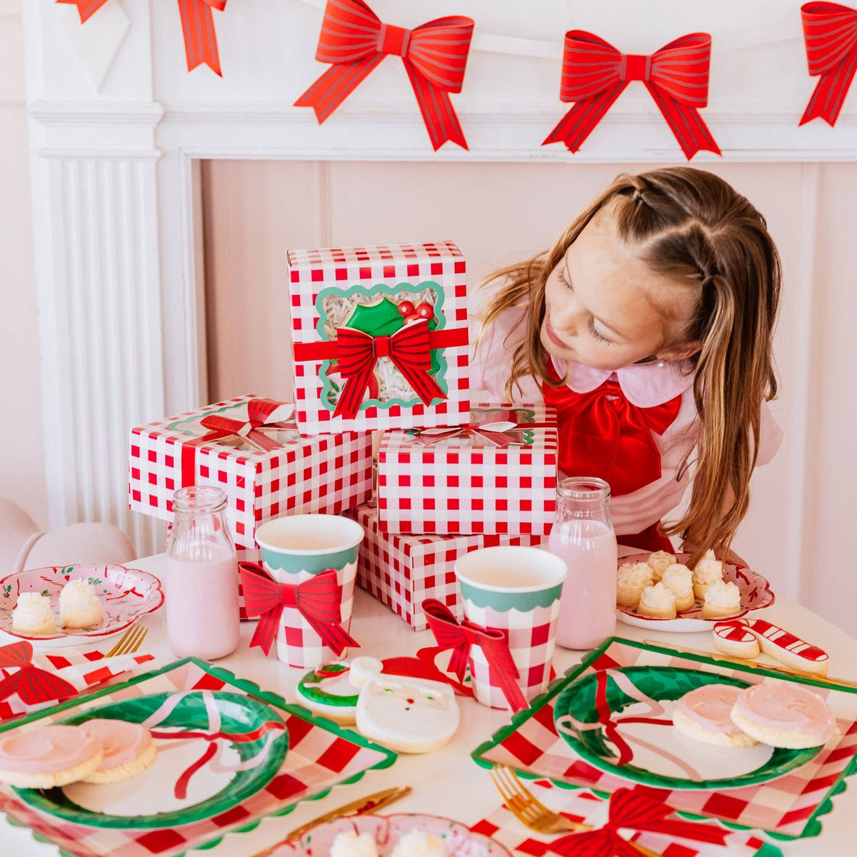 Girl setting Christmas table with red bow cookie boxes and milk bottles