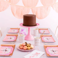 Pink birthday cake on a stand surrounded by ballerina dinner plates and balletcore party decor.