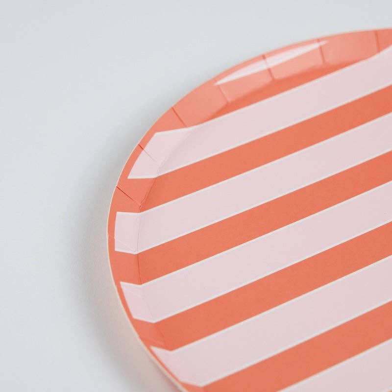 Close-up angled shot of the upper-right quadrant of the coral stripe dinner plate. Diagonal stripes in alternating coral-orange and pale pink run from upper left to lower right. The plate's crimped paper edge is visible where the stripes wrap over the rim.