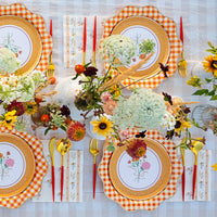 Outdoor fall table featuring orange gingham chargers and floral guest towels.