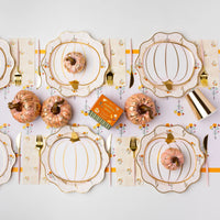 Long tablescape with cozy fall floral dinner plates layered under pumpkin plates, gold flatware, and mini pumpkins.