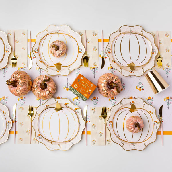 Long tablescape with cozy fall floral dinner plates layered under pumpkin plates, gold flatware, and mini pumpkins.