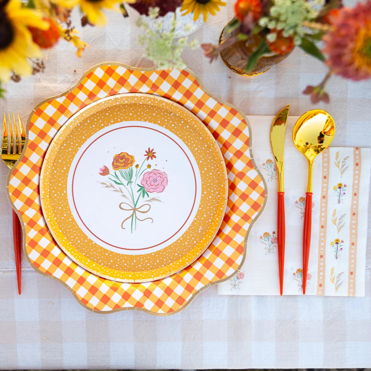 Close-up place setting showing orange gingham charger under a floral dessert plate with matching guest towel.