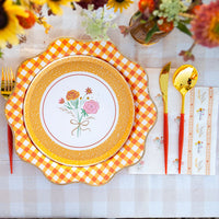 Close-up place setting showing orange gingham charger under a floral dessert plate with matching guest towel.