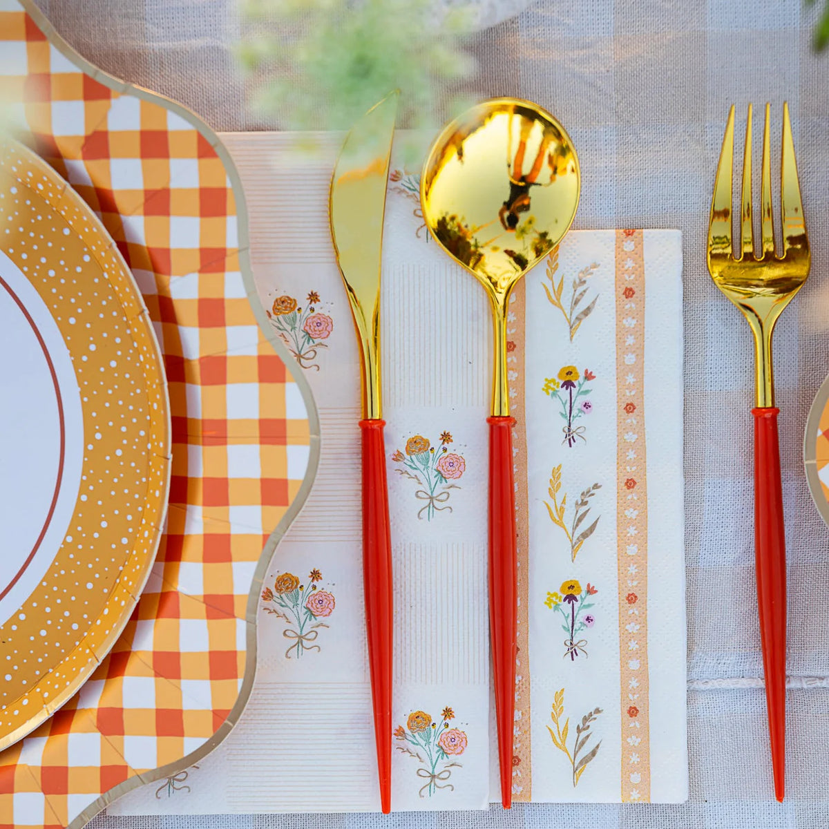 Close-up of gold flatware resting on a floral-stripe lunch napkin.