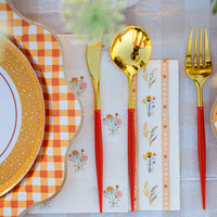 Close-up of gold flatware resting on a floral-stripe lunch napkin.