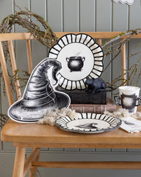 Halloween-themed table setting with halloween paper plates and a witch hat on a wooden table.